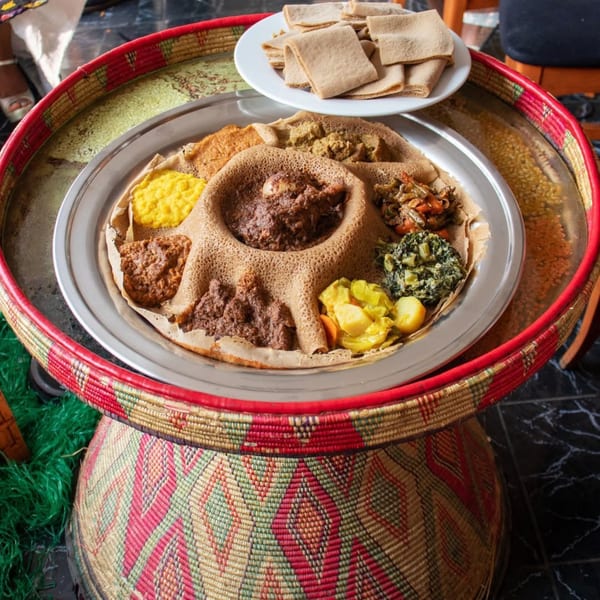 A large platter of Rosalind's Ethiopian injera bread and various stews on a woven basket table.