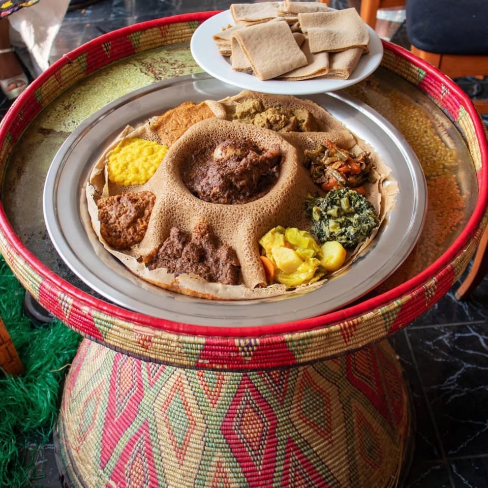 A large platter of Rosalind's Ethiopian injera bread and various stews on a woven basket table.