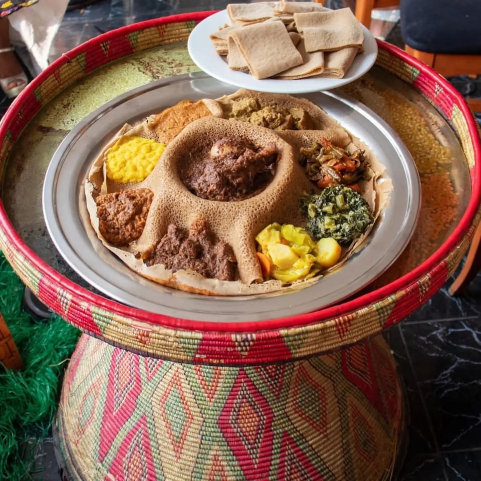 Rosalind's Ethiopian platter with injera, various stews, and vegetables on a woven table.