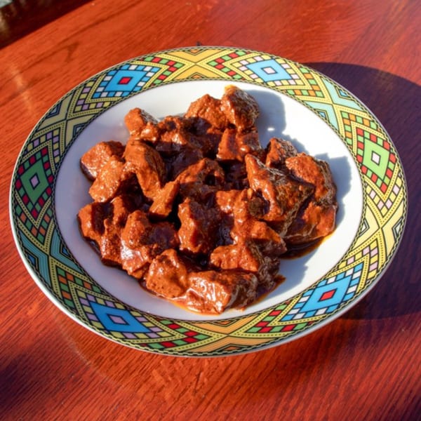 Rosalind's Ethiopian Tibs, a dish of cubed meat in a rich, dark red sauce, on a colorful patterned plate.