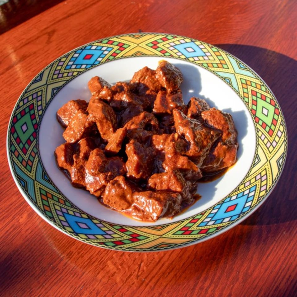 Rosalind's Ethiopian Tibs, a dish of cubed meat in a rich, dark red sauce, on a colorful patterned plate.