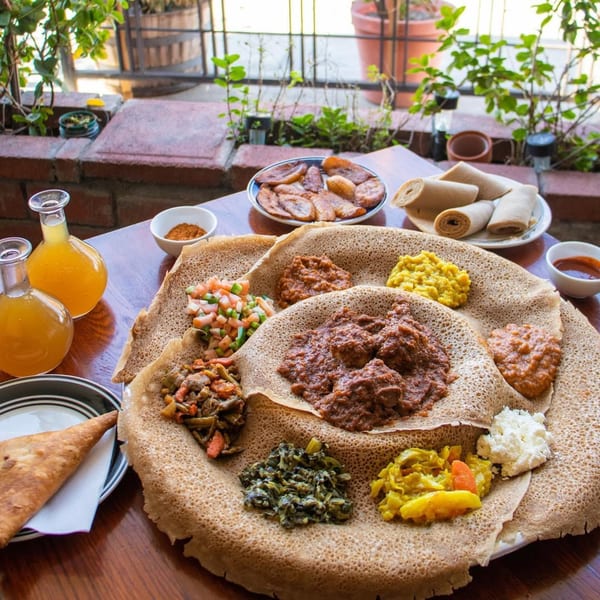 A large platter of Rosalind's Ethiopian injera bread with various stews and vegetables, plus drinks.